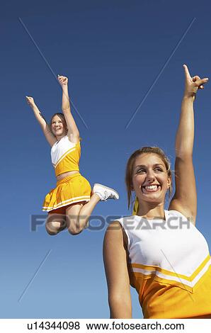 Stock Photo - Cheerleaders cheering and jumping, mid-air, low angle view. Fotosearch