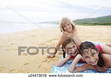 Stock Photo - Children reclining, hand on cheek on beach towel on sandy Beach. Fotosearch