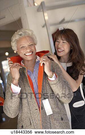 Stock Photograph - Clerk helping senior Woman try on jacket. Fotosearch