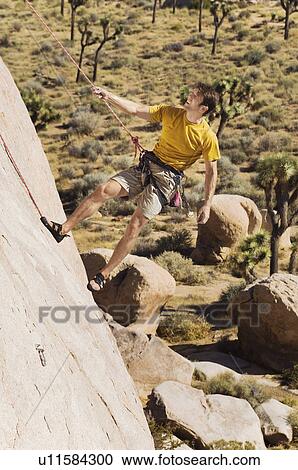 Stock Image - Climber Tugging on Rope on Cliff. Fotosearch