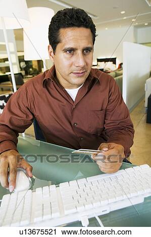 Stock Image - Concerned man running credit card through computer in furniture store. Fotosearch