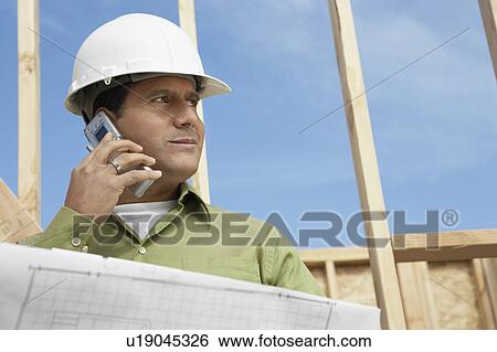 Stock Photograph - Construction Worker wearing hard hat, Using Cell Phone on construction site. Fotosearch