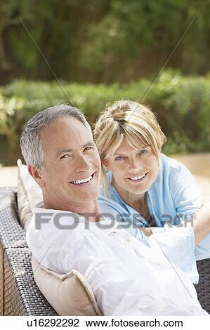 Stock Image - Contented middle-aged couple sitting outdoors on chairs, portrait. Fotosearch