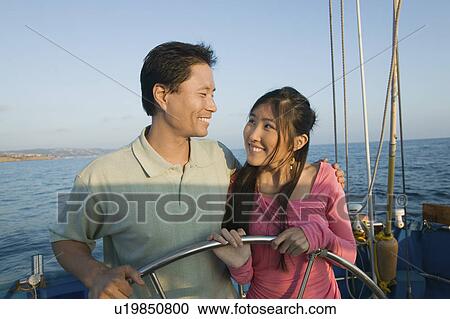 Stock Image - Couple at steering wheel of sailboat. Fotosearch