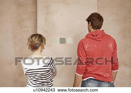 Stock Image - Couple choosing sample paint colours on wall, back view. Fotosearch