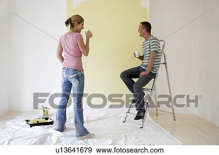 Couple drinking coffee and admiring freshly painted wall View Large Photo Image Stock Photo - Couple drinking coffee and admiring freshly painted wall. Fotosearch