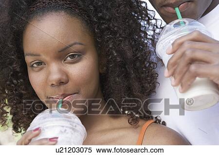 Stock Photography - Couple drinking milk shake from plastic cups, close-up of woman, (portrait). Fotosearch