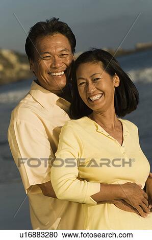 Stock Image - Couple embracing on beach, (portrait). Fotosearch