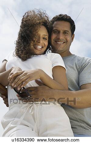 Stock Image - Couple embracing outdoors, (portrait), (low angle view). Fotosearch