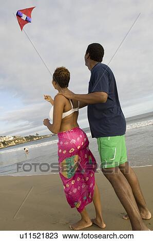 Stock Image - Couple flying kite on beach. Fotosearch