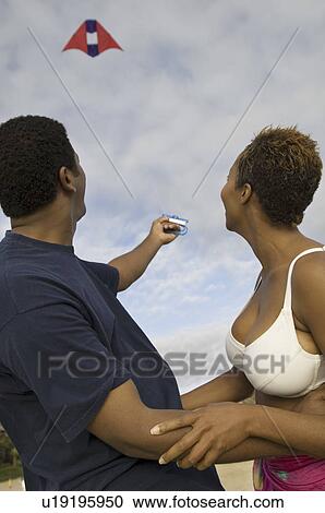 Stock Image - Couple flying kite, outdoors. Fotosearch