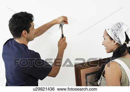 Stock Photograph - Couple hanging picture on interior wall, back view. Fotosearch