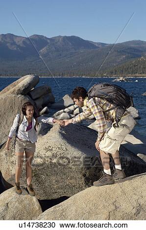 Stock Image - Couple hiking on boulders at coast. Fotosearch