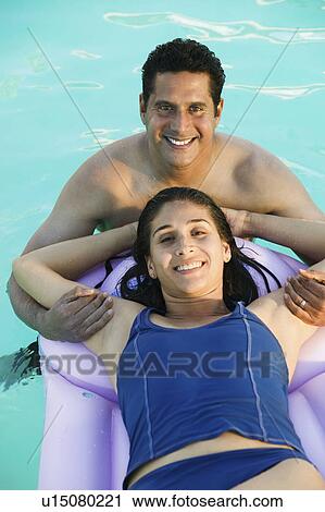 Stock Image - Couple in Swimming Pool, woman lying on inflatable raft, elevated view portrait.. Fotosearch