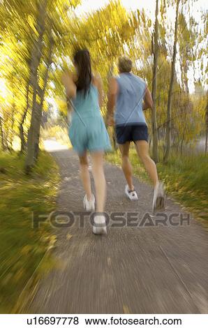 Stock Photo - Couple jogging through woods, rear view. Fotosearch