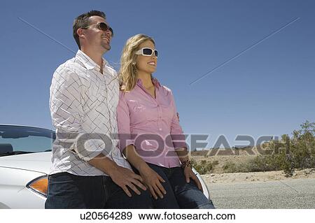 Stock Photo - Couple leaning on car in desert. Fotosearch