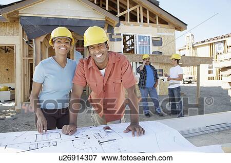 Stock Photo - Couple looking at blue prints of new house. Fotosearch