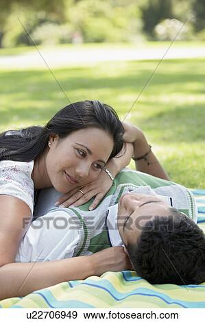 Stock Photo - Couple lying down together on blanket in park. Fotosearch