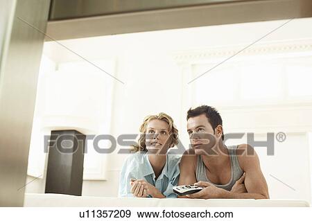 Stock Photo - Couple lying on bed together, man holding remote control. Fotosearch