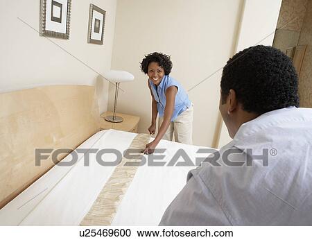 Stock Image - Couple making bed together. Fotosearch