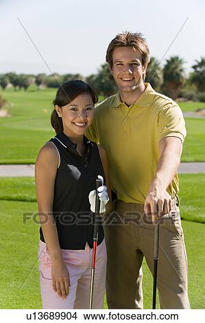 Couple of golfers standing together on golf course, (portrait) View Large Photo Image Picture - Couple of golfers standing together on golf course, (portrait). Fotosearch