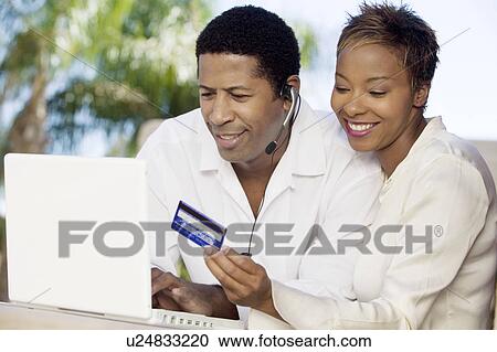 Stock Image - Couple on patio making online credit card purchase. Fotosearch