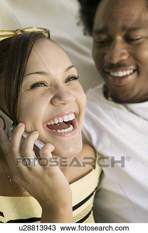 Stock Image - Couple on sofa, woman on cell phone laughing, close up. Fotosearch