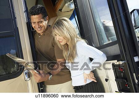 Stock Image - Couple outside RV looking through brochure. Fotosearch