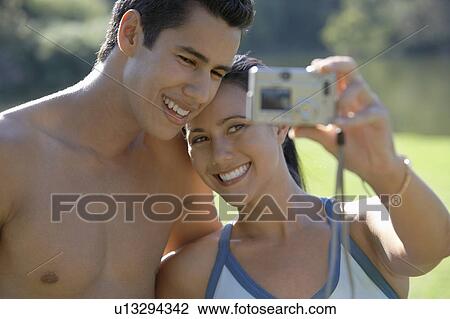 Couple photographing themselves, standing in park View Large Photo Image Stock Image - Couple photographing themselves, standing in park. Fotosearch
