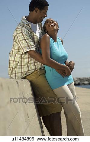 Stock Photograph - Couple relaxing by wall at beach. Fotosearch