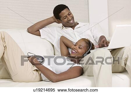 Stock Photography - Couple Relaxing on Couch with portable CD player and Laptop. Fotosearch