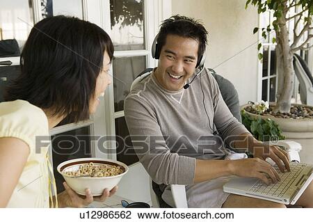 Stock Image - Couple relaxing on porch, man using laptop. Fotosearch
