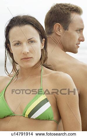 Picture - Couple sitting back to back on beach, portrait of woman, profile of man, close-up. Fotosearch