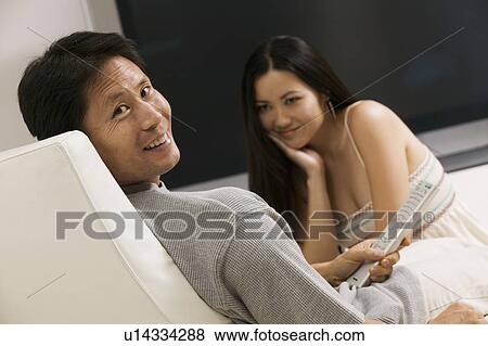 Stock Photo - Couple sitting by large flat screen television, portrait. Fotosearch