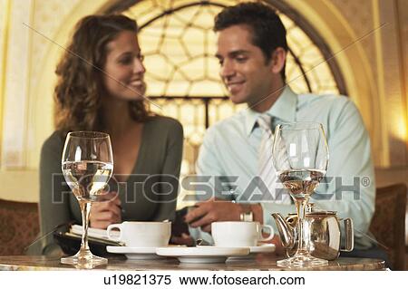 Couple sitting in cafe, woman holding daily organizer, wine glasses in foreground. View Large Photo Image Stock Photography - Couple sitting in cafe, woman holding daily organizer, wine glasses in foreground.. Fotosearch
