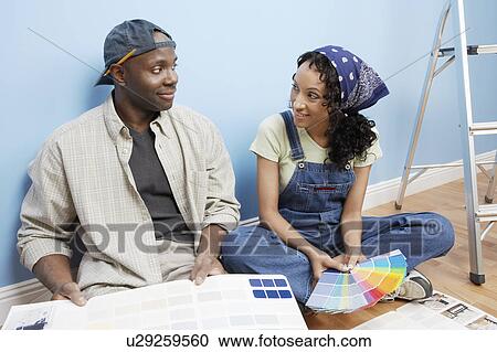 Stock Image - Couple sitting on floor of room looking at paint colour samples. Fotosearch
