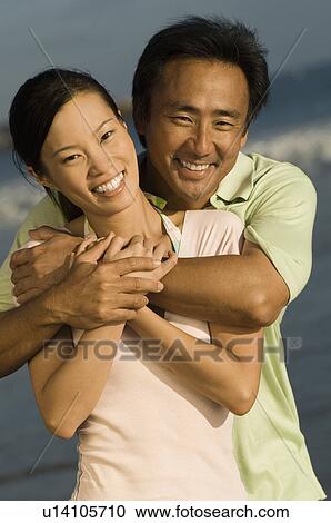 Stock Image - Couple smiling on beach, (portrait). Fotosearch