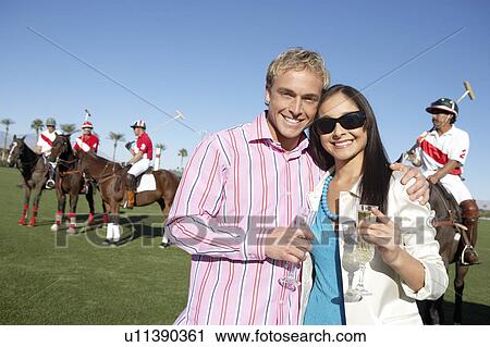 Couple standing, arms around, Celebrating with Champagne at a Polo Match View Large Photo Image Stock Image - Couple standing, arms around, Celebrating with Champagne at a Polo Match. Fotosearch