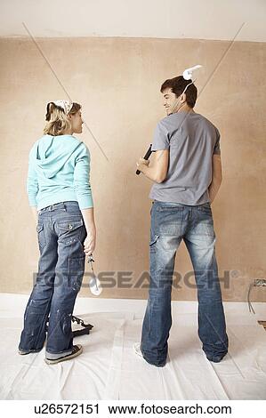Couple standing, holding paint rollers in unrenovated room, back view View Large Photo Image Stock Image - Couple standing, holding paint rollers in unrenovated room, back view. Fotosearch