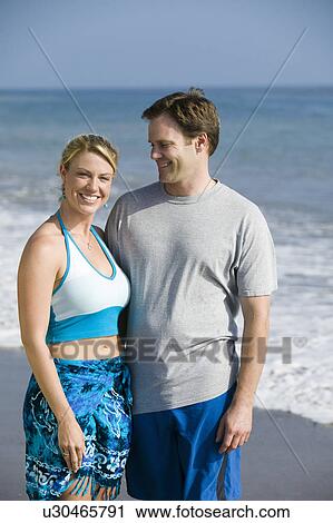 Stock Image - Couple standing on beach, portrait. Fotosearch