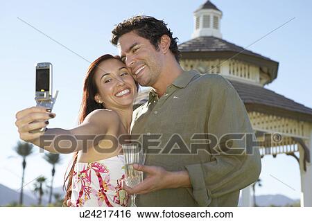 Stock Photograph - Couple Taking Photograph of themselves with Cell Phone near pavilion. Fotosearch