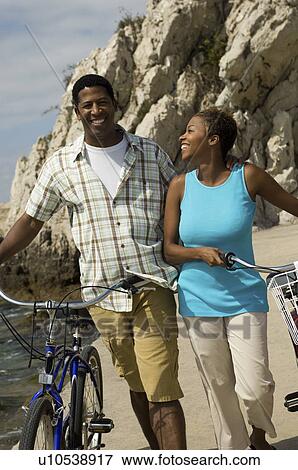 Stock Photo - Couple walking with bicycles at beach. Fotosearch