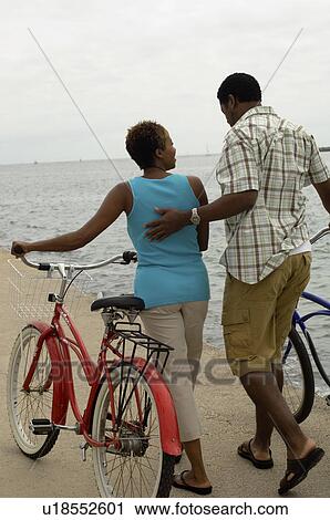 Stock Image - Couple walking with bicycles on beach. Fotosearch