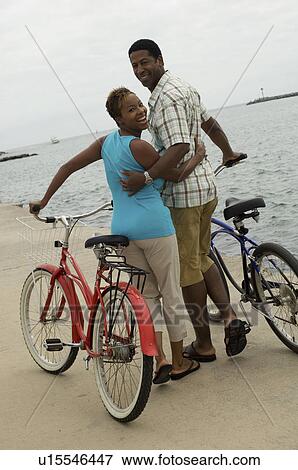 Stock Photo - Couple walking with bicycles on beach, (portrait). Fotosearch