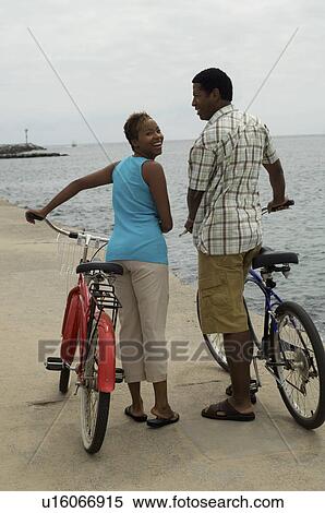Stock Photography - Couple walking with bicycles on beach. Fotosearch