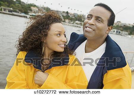 Stock Image - Couple wearing yellow anoraks on yacht. Fotosearch