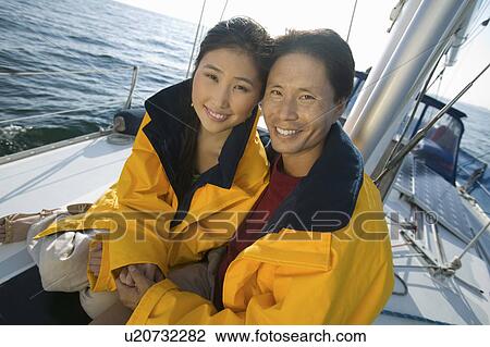 Stock Image - Couple wearing yellow anoraks on yacht, (portrait). Fotosearch