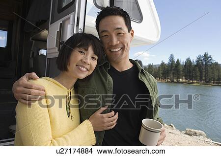 Picture - Couple with arms around each other outside RV at lake. Fotosearch