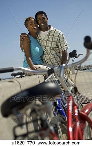 Couple with bicycles embracing on wall, (portrait) View Large Photo Image Stock Image - Couple with bicycles embracing on wall, (portrait). Fotosearch