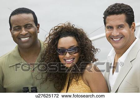 Stock Image - Couple with friend on yacht, (portrait). Fotosearch
